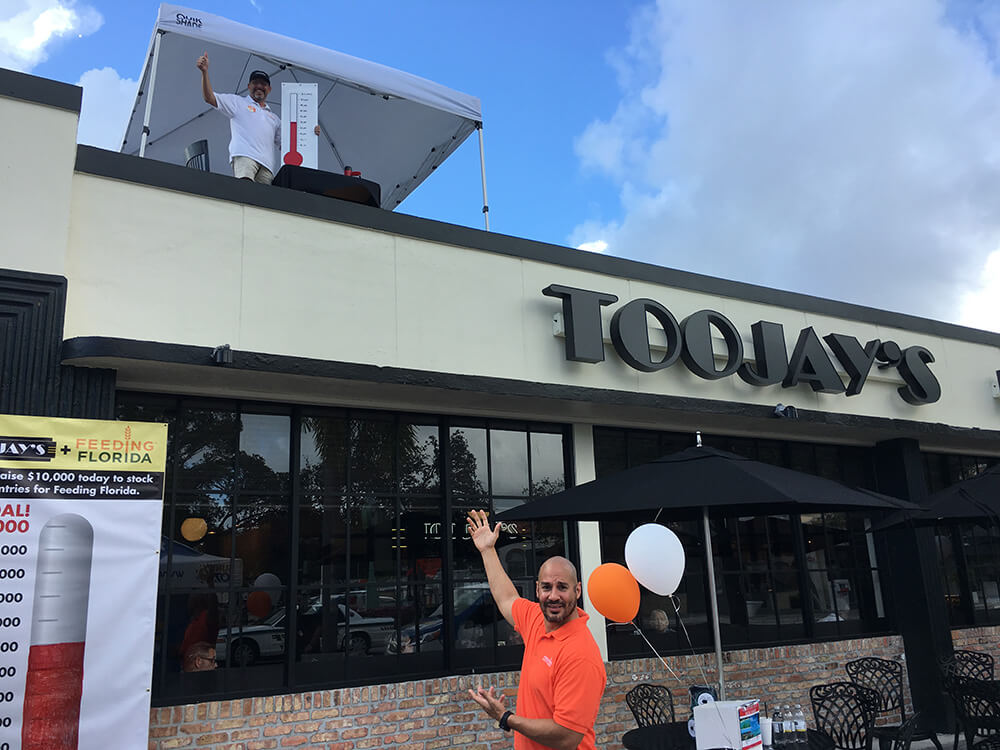 Feeding South Florida (a member of the Feeding Florida network of food banks) President and CEO Paco Vélez pointing to TooJay’s President and CEO Max Piet on top of the Lake Worth restaurant.